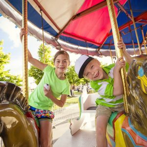Two cute kids enjoying a ride on a fun carnival carousel. A happy girl and boy are Smiling and having fun together at the summer carnival